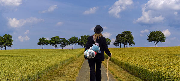 Junge Frau in Handwerkskluft auf der Walz läuft über einen Feldweg