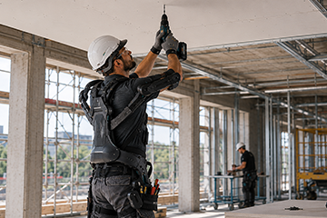 Handwerker auf Baustelle trägt Exoskelett und arbeitet über Kopf an einer Decke.