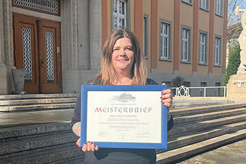 Rebecca Bürgi steht mit gerahmtem Meisterbrief in der Hand vor der Handwerkskammer Konstanz.