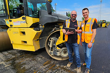 Zwei Straßenbauer mit Tablet vor einer großen Walzmaschine