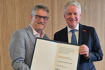 Georg Hiltner und Holger Schwannecke halten das Handwerkszeichen in Gold lächelnd in die Kamera.